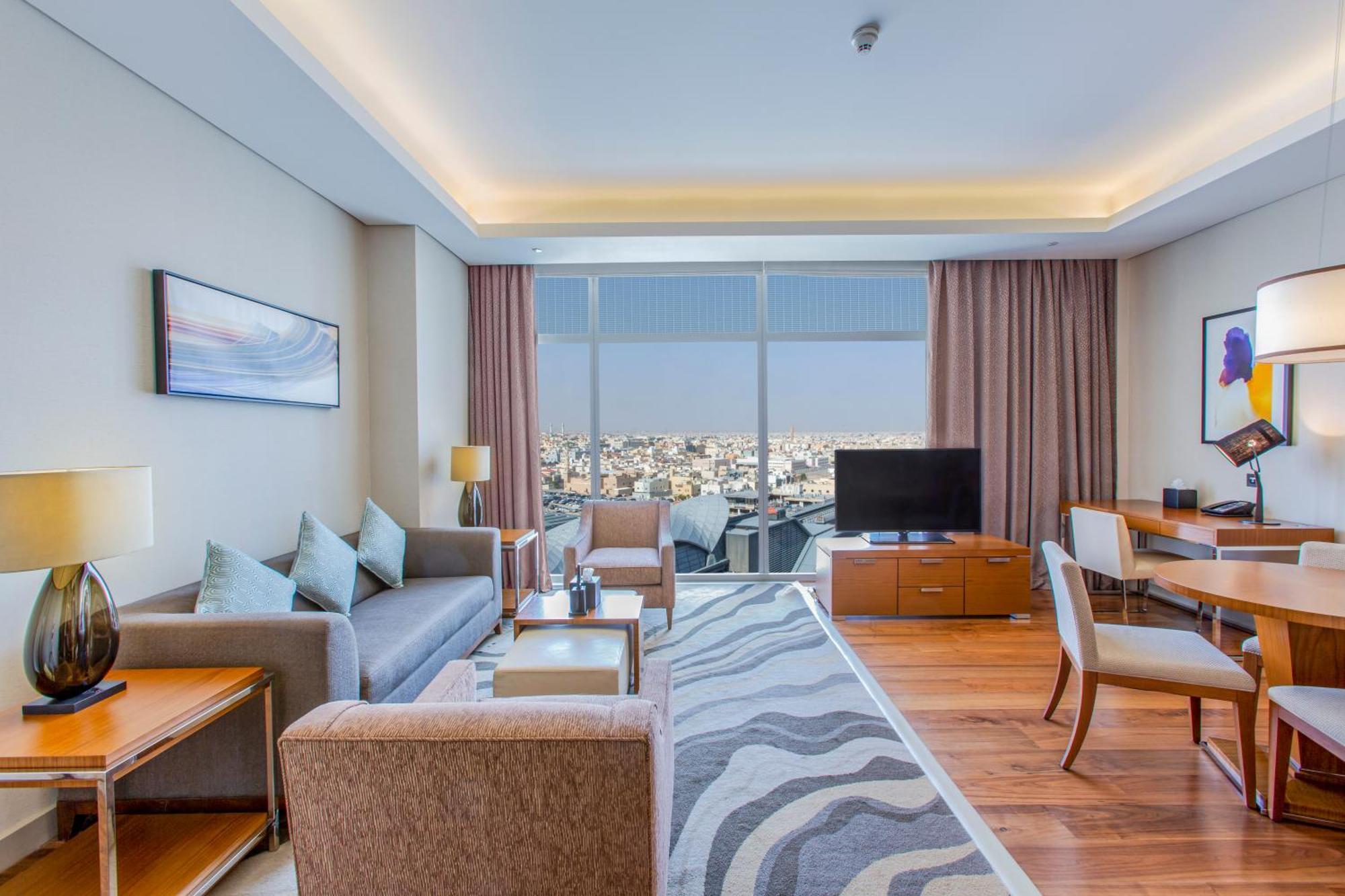 Hilton Riyadh Hotel & Residences Exteriör bild The photo shows a modern hotel room or suite. The space features a stylish living area with a sofa and armchairs arranged around a coffee table. There are lamps providing ambient lighting, and a large window offers a view of the cityscape outside. A 