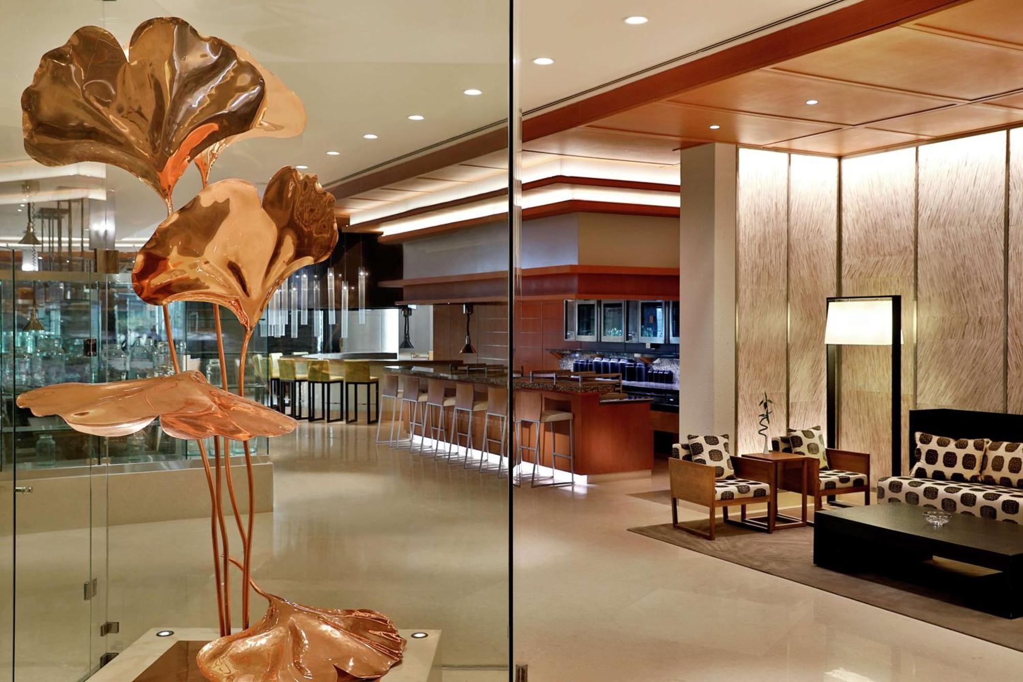 Hilton Riyadh Hotel & Residences Exteriör bild The photo depicts a modern and stylish interior space, likely a hotel lobby or upscale lounge. In the foreground, there is an artistic sculpture of copper-colored leaves or flowers, adding an elegant touch. The background features a well-lit bar area