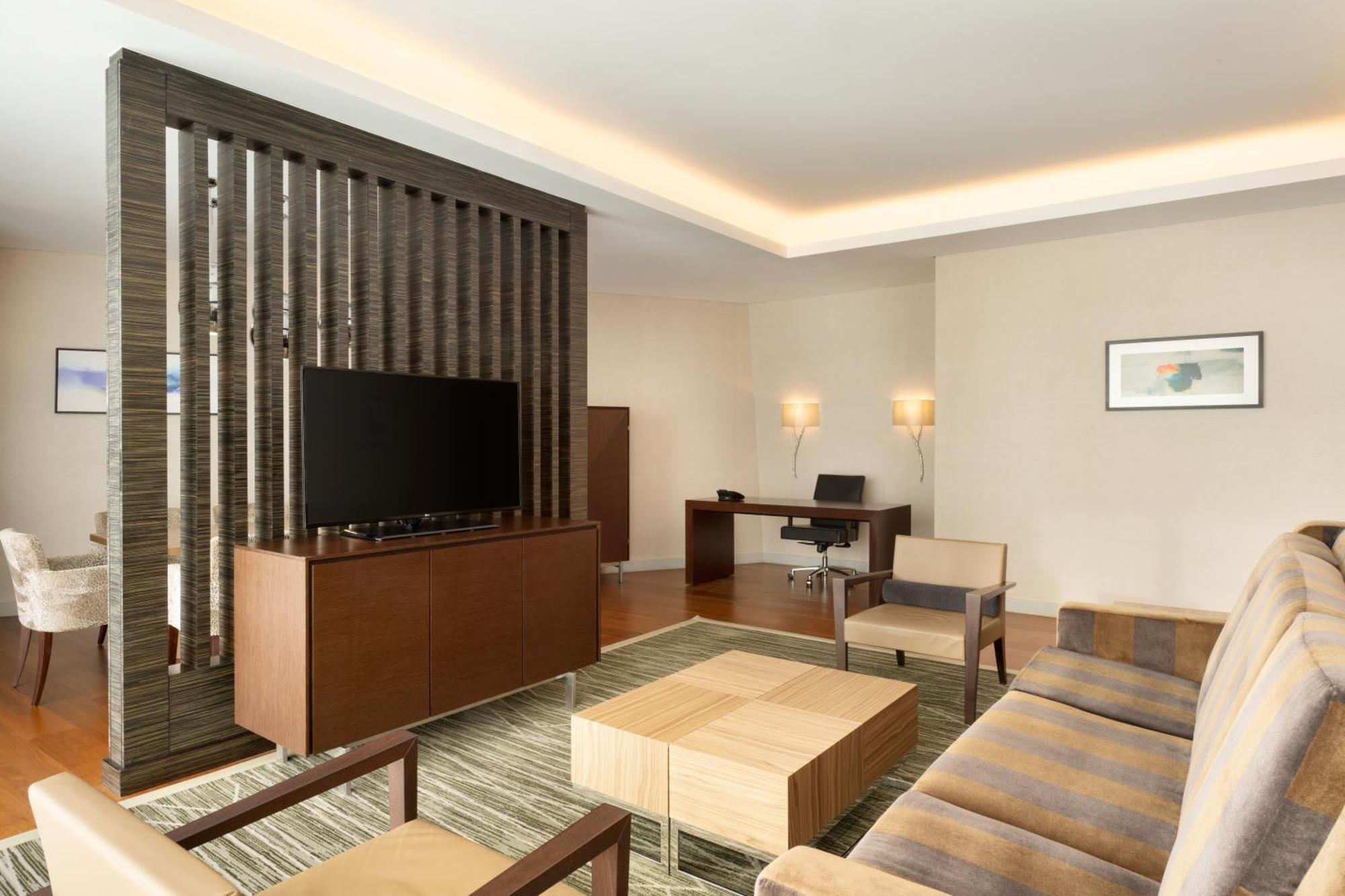 Hilton Riyadh Hotel & Residences Exteriör bild The photo shows a modern living space that features a contemporary design. It includes a seating area with a beige sofa and two armchairs arranged around a square wooden coffee table. A wall-mounted flat-screen TV is positioned on a decorative wooden