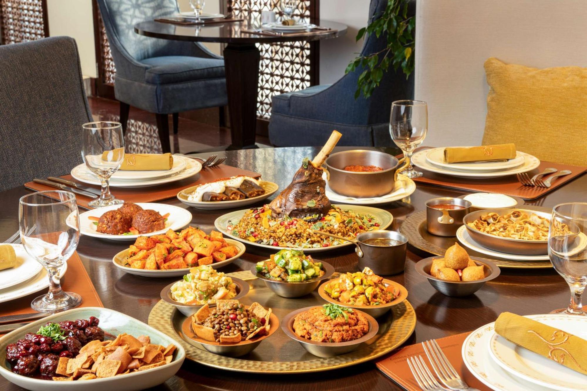 Hilton Riyadh Hotel & Residences Exteriör bild The photo depicts a beautifully arranged dining table featuring a variety of dishes. There are several large plates filled with different foods, including a prominent dish at the center that appears to be rice and meat, likely a type of biryani or pi